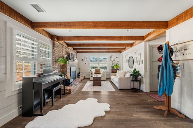 living area featuring beam ceiling, visible vents, a fireplace, and wood finished floors