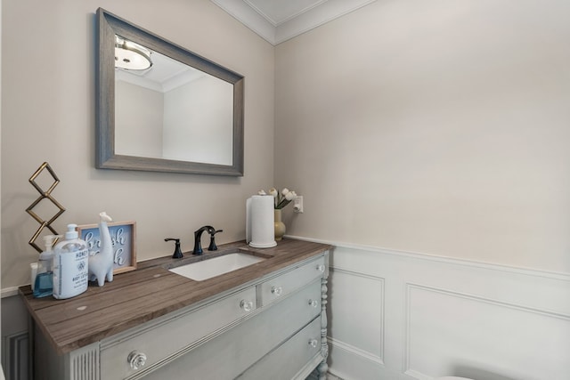 bathroom featuring vanity, a decorative wall, a wainscoted wall, and ornamental molding