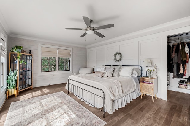 bedroom with dark wood-style floors, a decorative wall, a ceiling fan, and ornamental molding