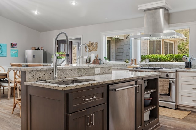 kitchen with light stone countertops, light wood-style flooring, island exhaust hood, a sink, and stainless steel appliances