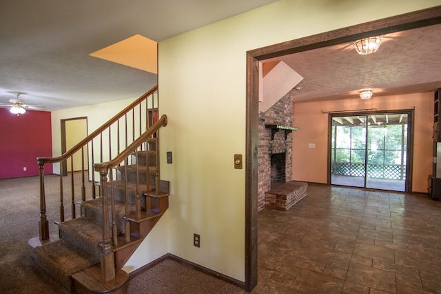 stairway featuring ceiling fan, a textured ceiling, and a brick fireplace