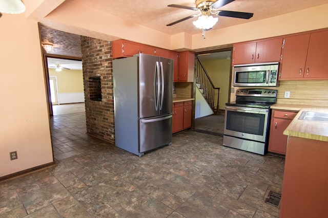 kitchen featuring ceiling fan, stainless steel appliances, brick wall, backsplash, and a textured ceiling