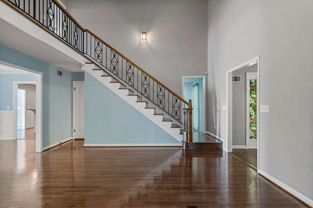 entryway with stairs, a high ceiling, visible vents, and wood finished floors