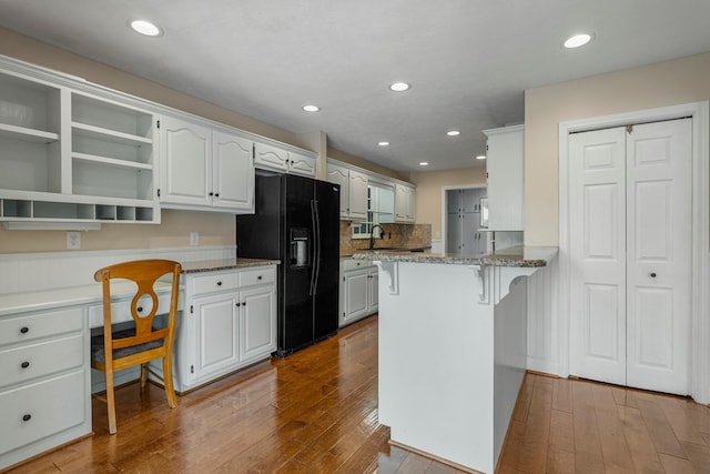 kitchen featuring a kitchen breakfast bar, open shelves, black fridge, and hardwood / wood-style floors