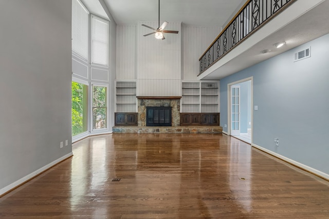 unfurnished living room with visible vents, a towering ceiling, a fireplace, baseboards, and a ceiling fan