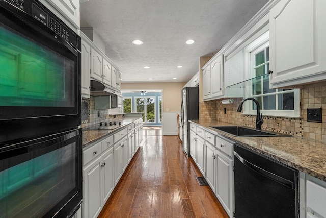 kitchen featuring white cabinets, light stone counters, a sink, under cabinet range hood, and black appliances