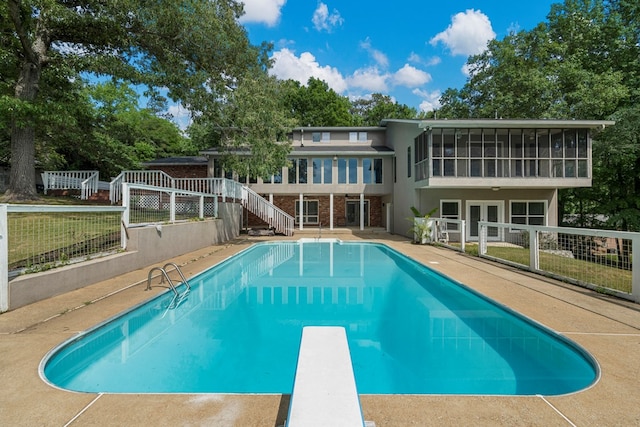 outdoor pool featuring fence, a diving board, a sunroom, stairway, and french doors
