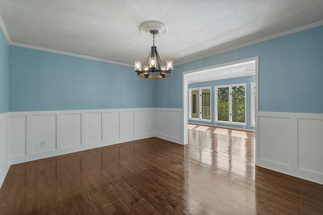 spare room featuring wainscoting, crown molding, a decorative wall, and a chandelier
