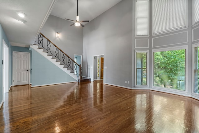 unfurnished living room featuring stairway, a high ceiling, a ceiling fan, and wood finished floors