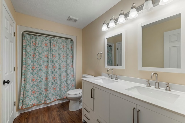 full bath with double vanity, toilet, a sink, and wood finished floors