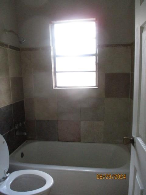 bathroom with tiled shower / bath combo and toilet