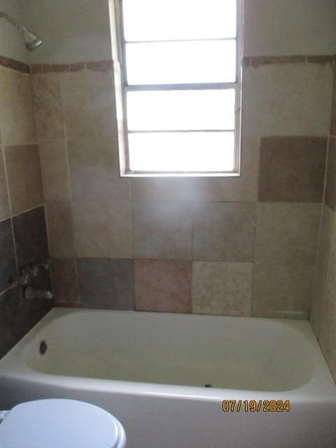 bathroom with toilet and tiled shower / bath