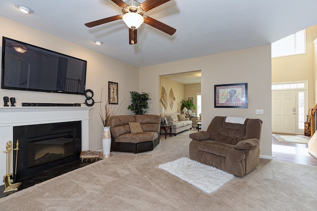 carpeted living room featuring a textured ceiling, ceiling fan, and a fireplace with flush hearth