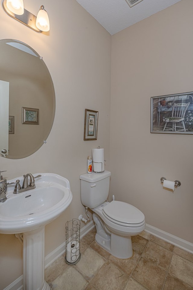 half bath featuring baseboards, visible vents, and toilet