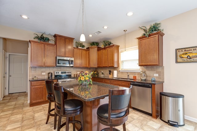 kitchen featuring a kitchen island, visible vents, appliances with stainless steel finishes, brown cabinets, and a kitchen bar