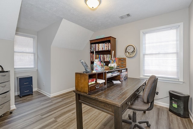 home office with a healthy amount of sunlight, visible vents, light wood finished floors, and a textured ceiling