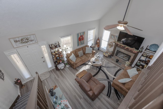 living room with vaulted ceiling, a fireplace, wood finished floors, a textured ceiling, and a ceiling fan