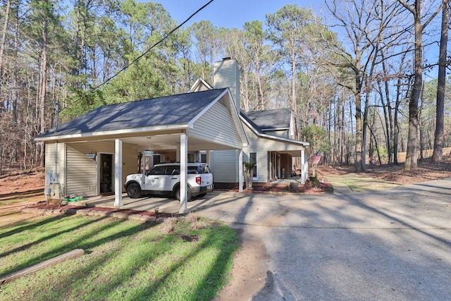 view of side of property featuring driveway, a porch, a yard, a chimney, and a carport