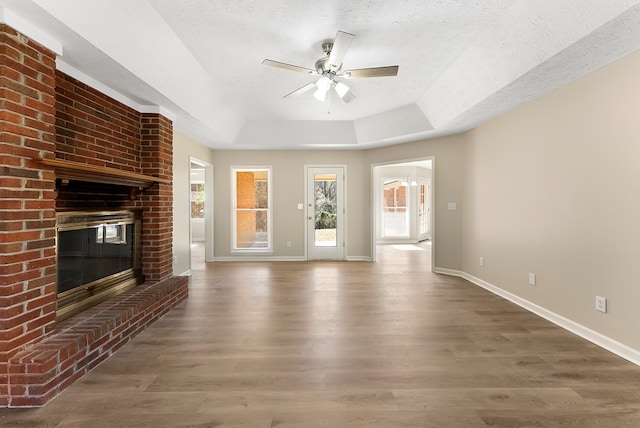 unfurnished living room with ceiling fan, dark hardwood / wood-style floors, a textured ceiling, a brick fireplace, and a raised ceiling