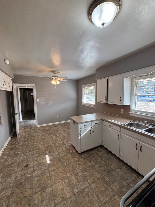 kitchen with a wealth of natural light, white cabinetry, kitchen peninsula, and sink