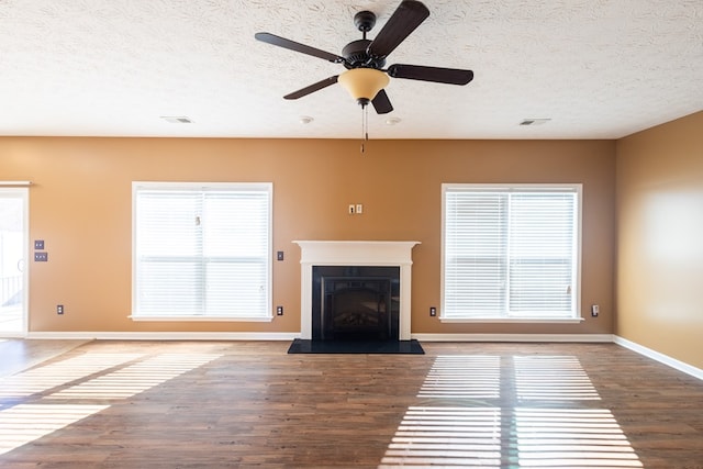 unfurnished living room featuring baseboards, visible vents, a fireplace with raised hearth, wood finished floors, and a textured ceiling