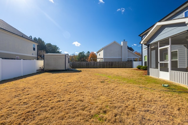 view of yard with a sunroom, a fenced backyard, an outbuilding, and a shed