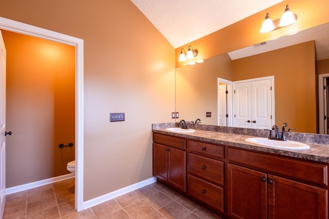 bathroom with double vanity, baseboards, toilet, vaulted ceiling, and a sink