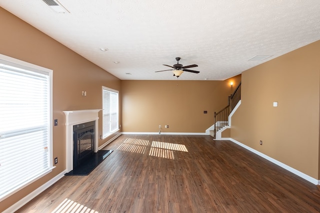 unfurnished living room with dark wood finished floors, visible vents, baseboards, stairway, and a glass covered fireplace