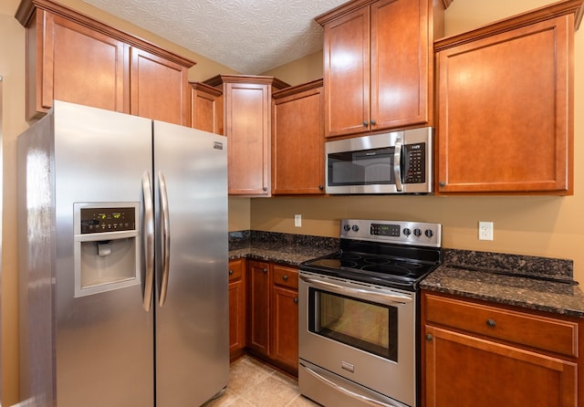 kitchen featuring brown cabinets, dark stone counters, stainless steel appliances, and a textured ceiling