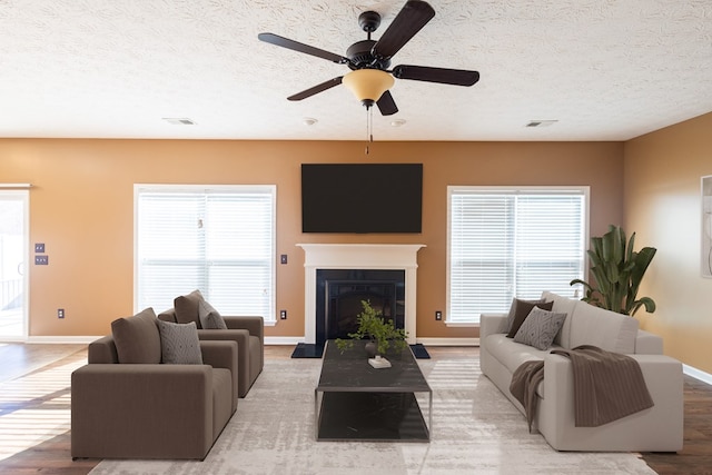 living area featuring a textured ceiling, visible vents, a fireplace with raised hearth, and wood finished floors