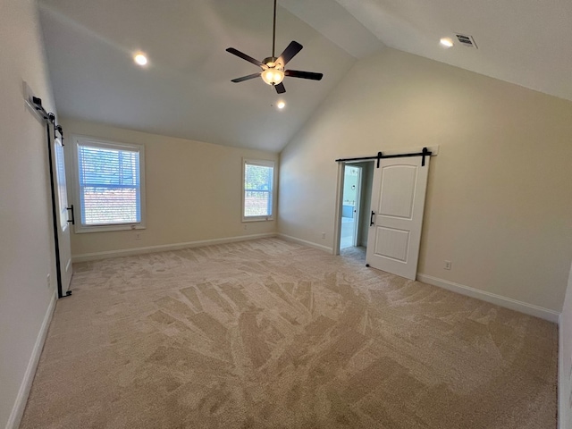 unfurnished bedroom with ceiling fan, light colored carpet, a barn door, and high vaulted ceiling