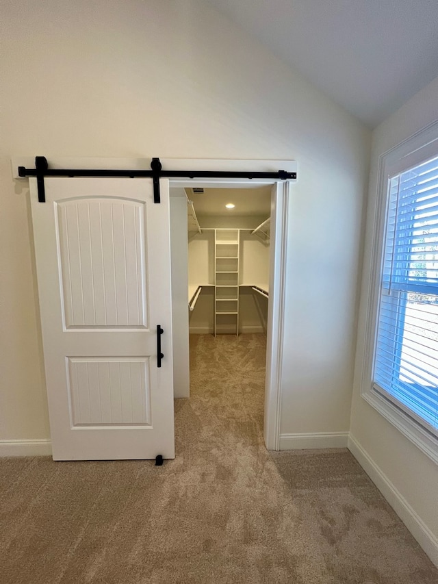 spacious closet with lofted ceiling, light colored carpet, and a barn door