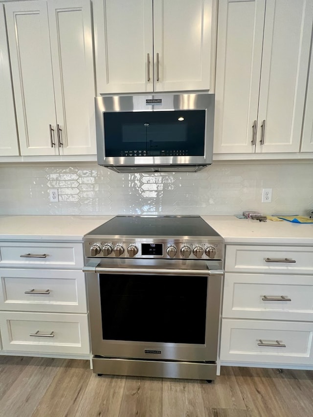 kitchen featuring stainless steel appliances, backsplash, white cabinets, and light wood-type flooring