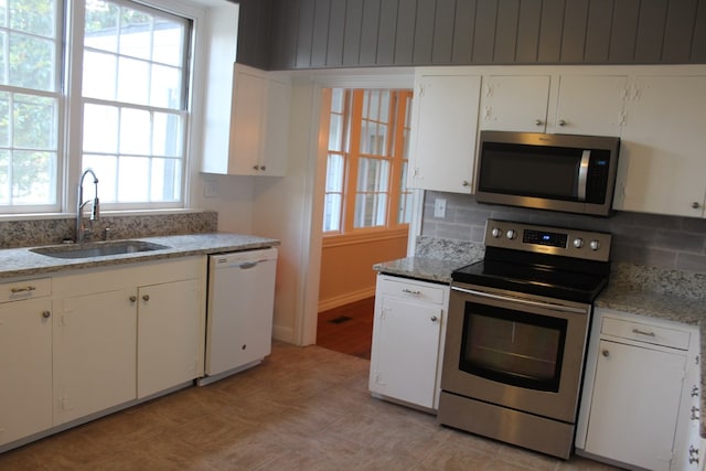 kitchen with appliances with stainless steel finishes, a sink, white cabinetry, decorative backsplash, and light stone counters