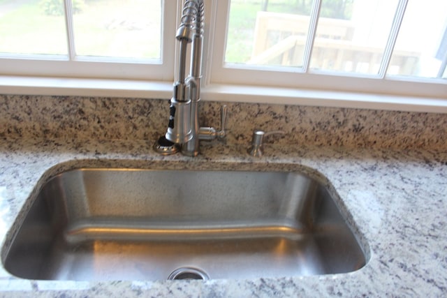 kitchen view of a sink, light stone counters, and decorative backsplash