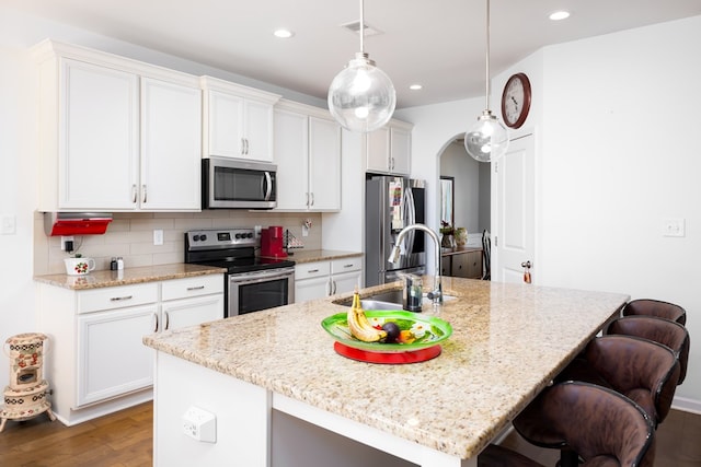 kitchen featuring stainless steel appliances, dark hardwood / wood-style floors, decorative light fixtures, a breakfast bar area, and a kitchen island with sink