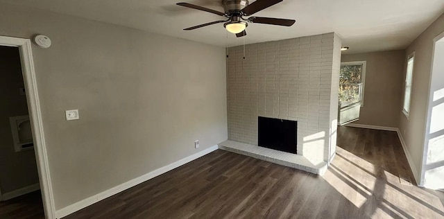 unfurnished living room with dark wood-style floors, a brick fireplace, ceiling fan, and baseboards