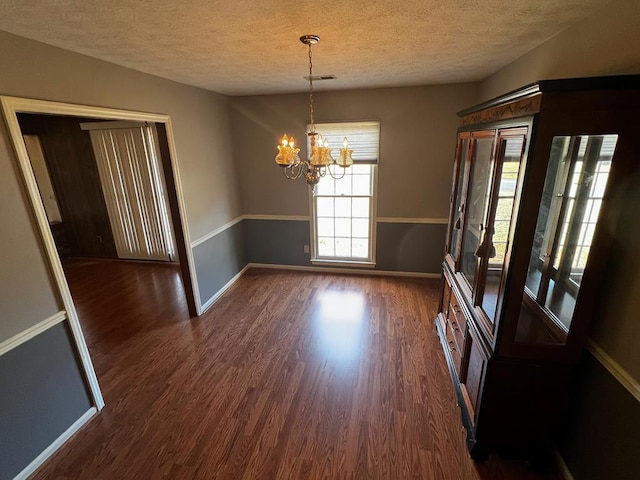 unfurnished dining area featuring a textured ceiling, a chandelier, and dark hardwood / wood-style floors