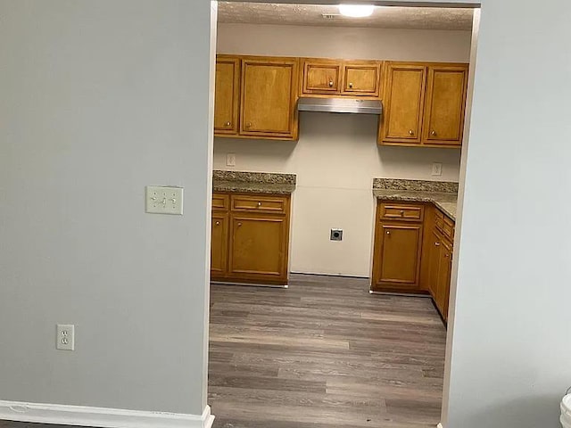 3514 Youmans St, Columbus, GA 31903 - kitchen with brown cabinetry, wood finished floors, under cabinet range hood, and dark stone countertops
