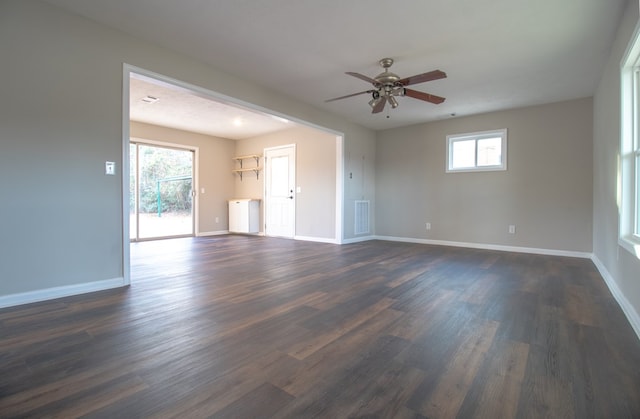 empty room with ceiling fan, a healthy amount of sunlight, and dark hardwood / wood-style flooring