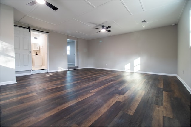 spare room with dark hardwood / wood-style floors, ceiling fan, and a barn door