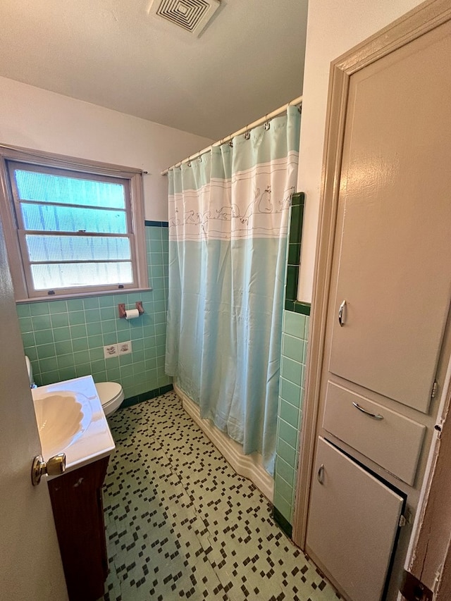 bathroom featuring toilet, curtained shower, visible vents, and tile walls