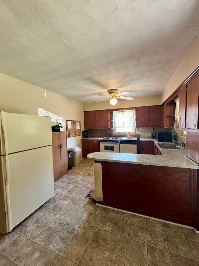 kitchen featuring a peninsula, white appliances, a sink, a ceiling fan, and light countertops