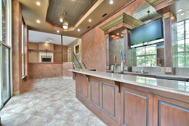 kitchen with dishwashing machine, light stone counters, a sink, open floor plan, and a tray ceiling