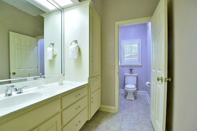 bathroom with a skylight, toilet, vanity, tile patterned flooring, and baseboards