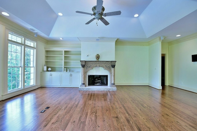 unfurnished living room featuring a tray ceiling, wood finished floors, and a high end fireplace