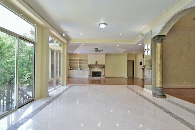 unfurnished living room featuring built in shelves, arched walkways, crown molding, a fireplace with raised hearth, and baseboards