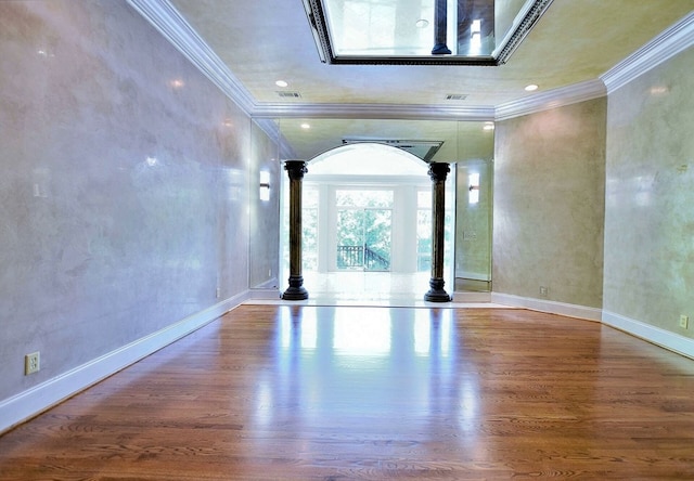 spare room with decorative columns, baseboards, arched walkways, wood finished floors, and crown molding