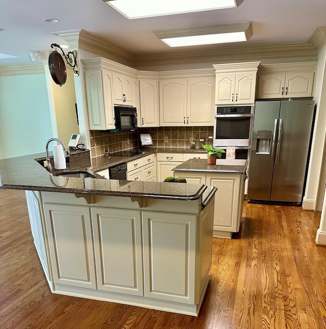 kitchen featuring a peninsula, wood finished floors, a kitchen island, black appliances, and tasteful backsplash