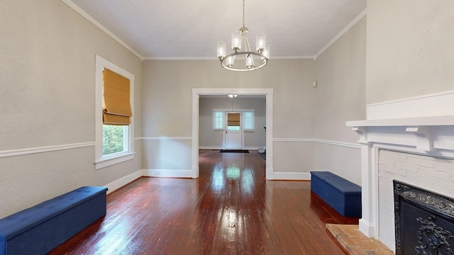 unfurnished dining area with hardwood / wood-style floors, a chandelier, a fireplace with raised hearth, baseboards, and crown molding